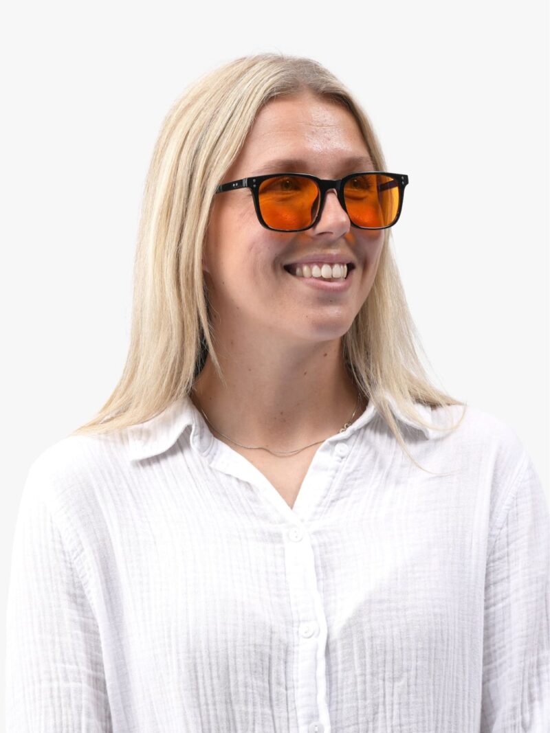 Lächelnde Frau im weißen Hemd mit der schwarzen Obsidian 90 Brille mit orangefarbenen Gläsern