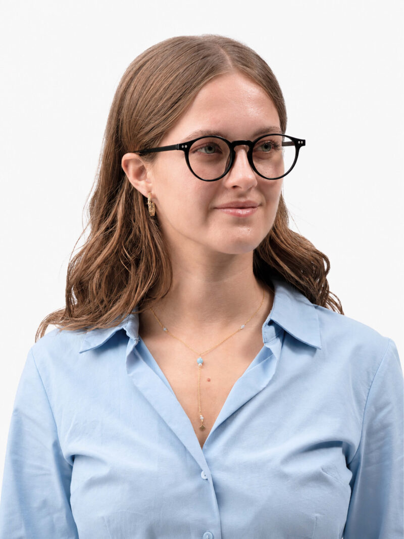Porträt einer Frau mit schwarzen runden Brillen, goldener Kette, hellblauer Bluse und leichtem Lächeln