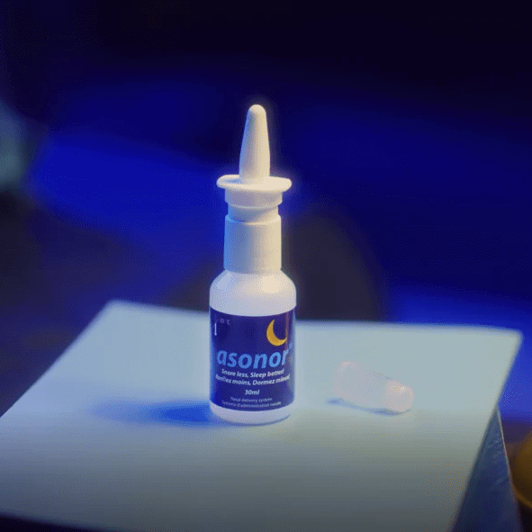 Weiße Nasenspray-Flasche mit blauem Asonor Etikett und Mondsymbol auf einem Tisch, Verschlusskappe daneben, blaues Hintergrundlicht