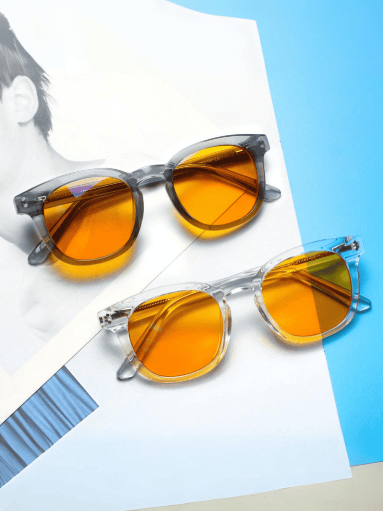 Zwei transparente Sonnenbrillen mit orangefarbenen Gläsern vor weißem und blauem Hintergrund