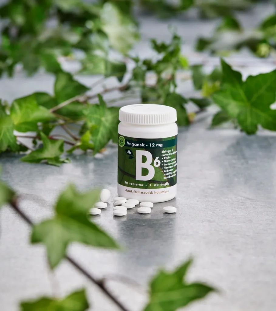 Dose mit Vitamin-B6-Tabletten, weiße Tabletten davor verstreut und grüne Blätter im Hintergrund