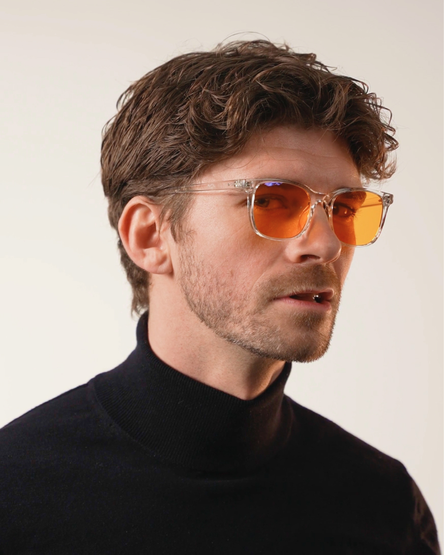 Mann im Dreiviertelprofil mit lockigem dunkelbraunem Haar und transparenter, orange getönter Brille, im schwarzen Rollkragenpullover