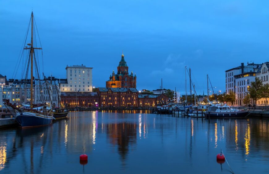 Abendlicher Hafen von Helsinki mit beleuchteter Uspenski-Kathedrale, Booten und Lichterreflexionen