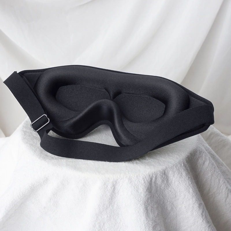 Gepolsterte 3D-Schlafmaske in Schwarz mit geformten Augenmulden und verstellbarem Gummiband auf weißem Tuch