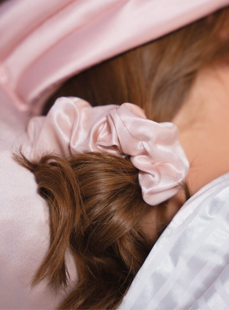 Braunes Haar zusammengebunden mit rosafarbenem Satin-Scrunchie auf hellem Kissen