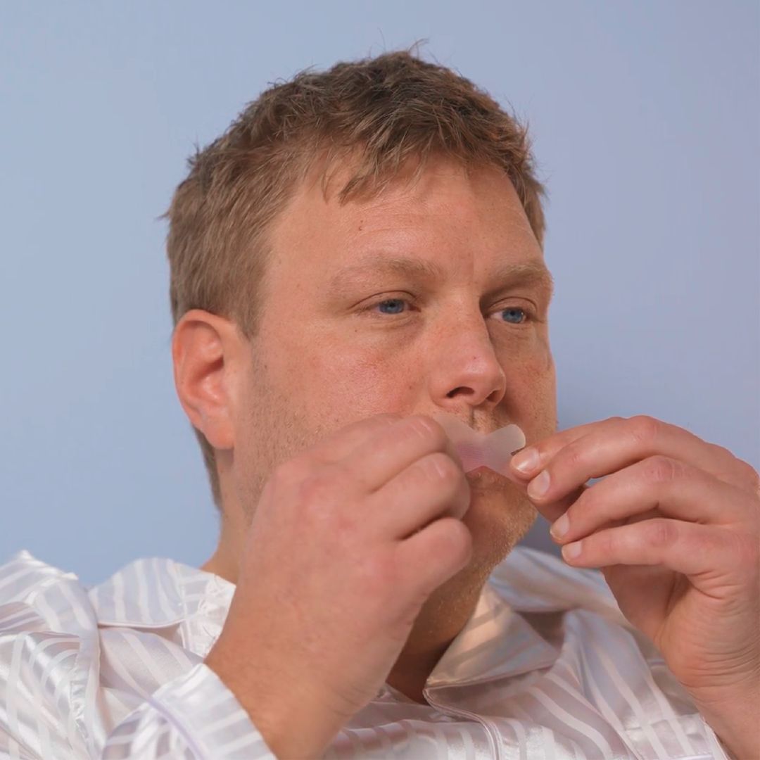 Mann in Pyjama klebt Mundtape über die Lippen