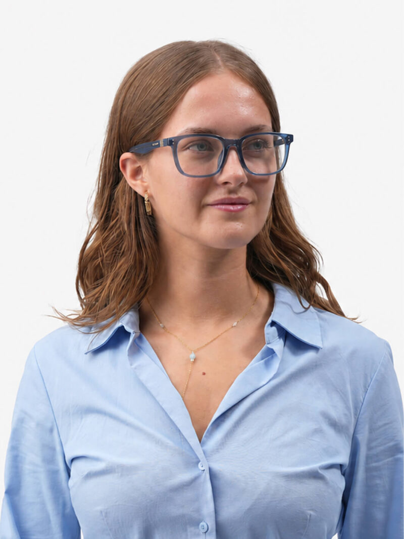 Junge Frau mit blauer Brille und hellblauer Bluse, goldene Kette und Ohrring, leicht lächelnd, nach rechts blickend