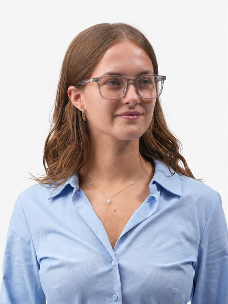 Porträt einer Frau mit hellgrauem Brillengestell, goldener Halskette und offenem hellblauen Hemd, leicht lächelnd