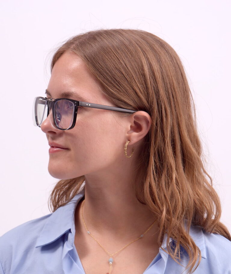 Frau im Profil mit Blaulichtfilter-Brille, goldener Creole, hellblauem Hemd und zarter Halskette